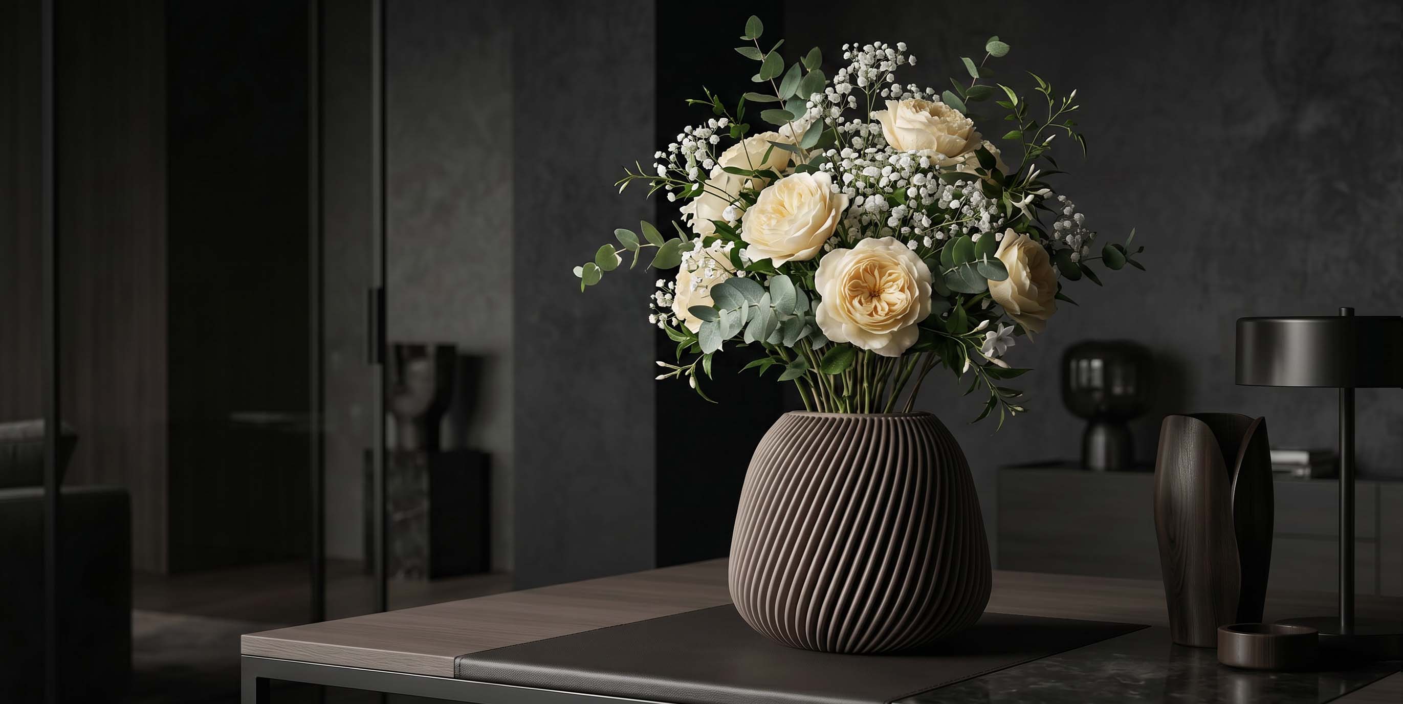 Strauß mit weißen Rosen und Eukalyptuszweigen in einer gerippten Vase auf einem Tisch im dunklen Raum.