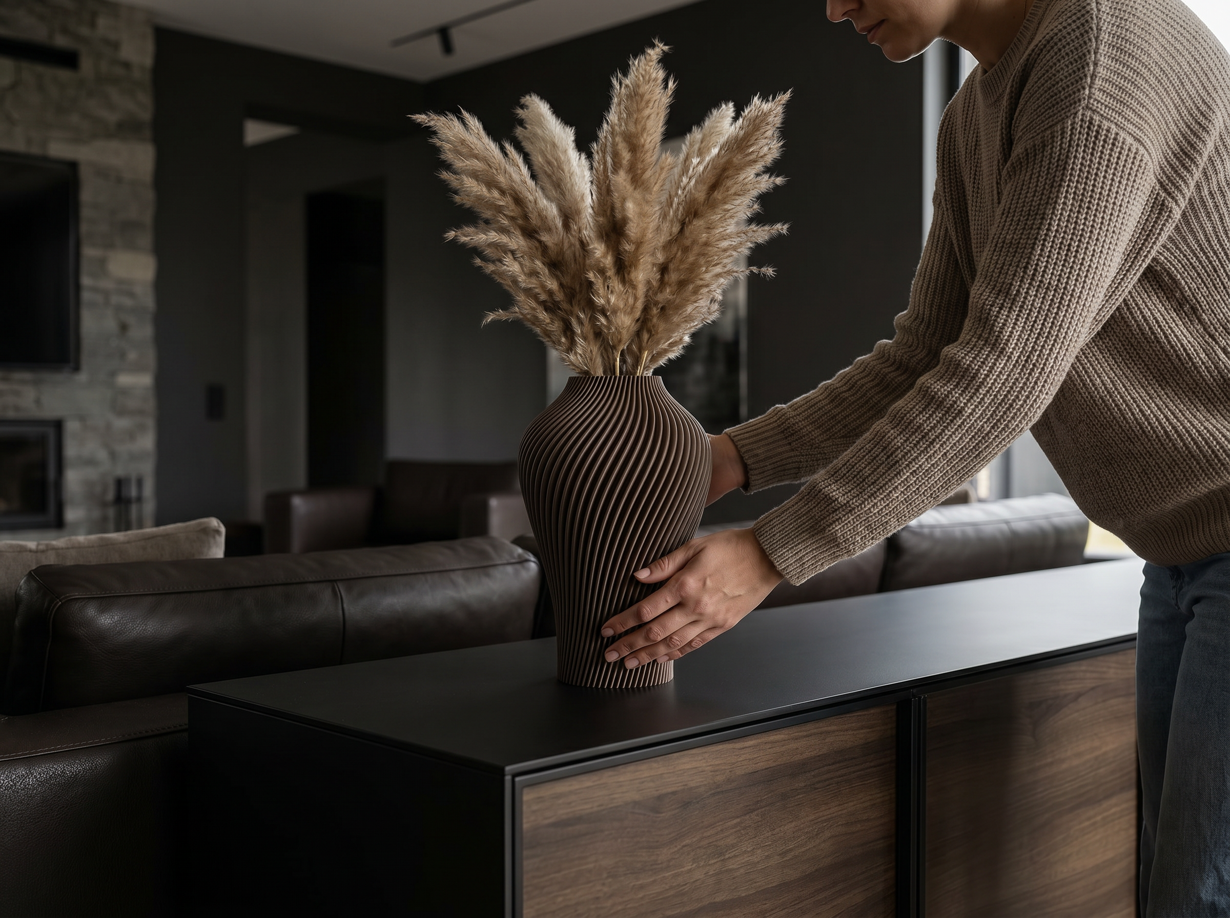 Eine Person stellt eine braune, gerippte Vase mit Pampasgras auf den Couchtisch im Wohnzimmer.