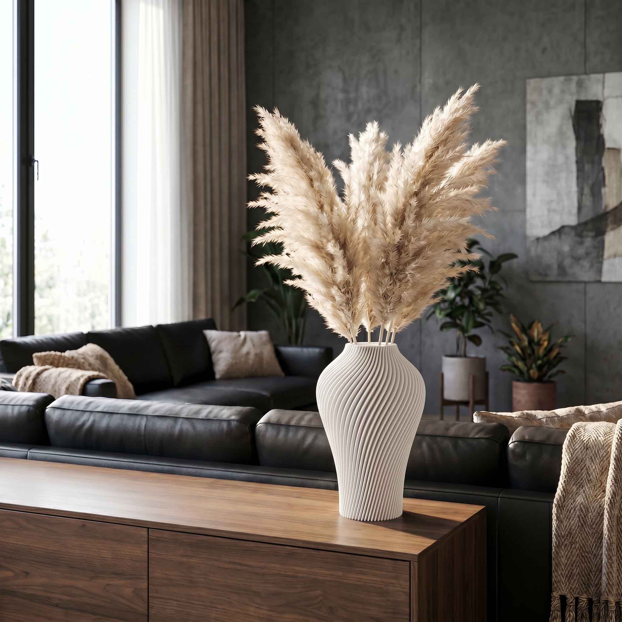 Pampasgras in einer gestreiften weißen Vase steht vor einem Sofa, im Hintergrund Fensterlicht und graue Wand.